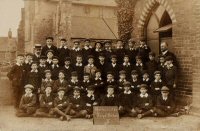 This seems to be a photograph of class II, Somercotes Boys School taken outside the School House with the Church of St. Thomas in the background. It probably dates from the early 1900s.